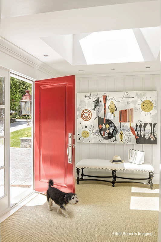Bright red front door opened to a small black dog walking through it, with colorful art displayed on the wall. 