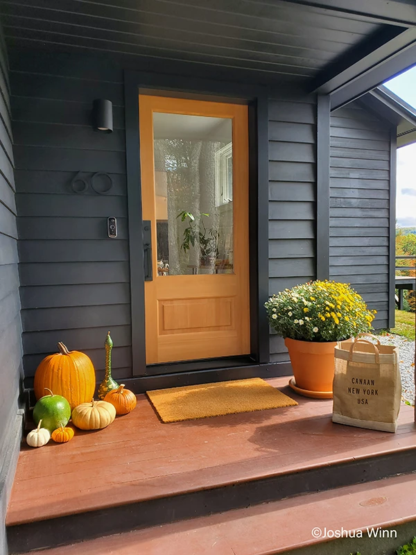 Wood front door with glass contrasted to a black exterior and fall décor on the front porch.