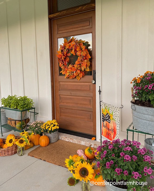 Front door decorated with a fall wreath and pumpkins and flowers on the front porch.